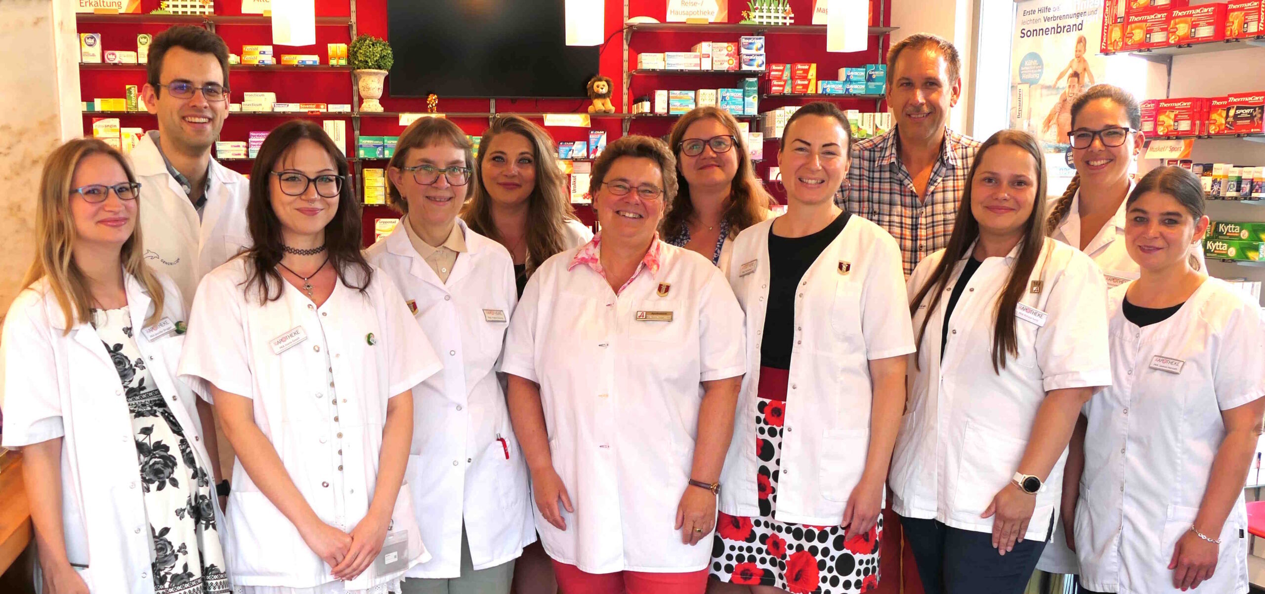 Abbildung zeigt Mitarbeiter der Apotheke Ebenfurth im Verkaufsraum der von der Farbe ROT dominiert wird. Alle schauen freundlich und wollen die Kunden bedienen.